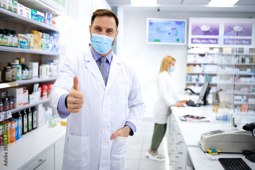 Portrait of handsome caucasian male pharmacist with face mask standing in pharmacy store.