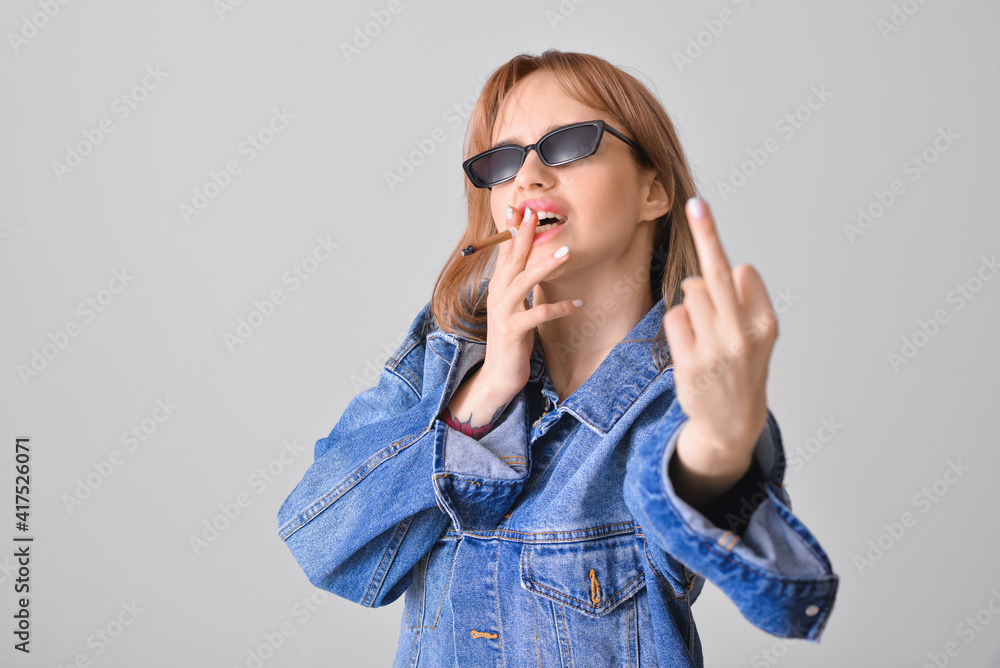Young smoking woman showing middle finger on grey background
