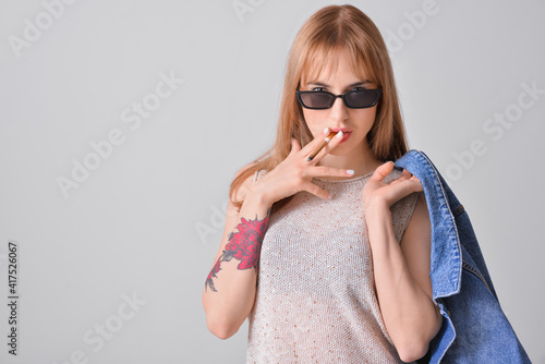 Young smoking woman on grey...