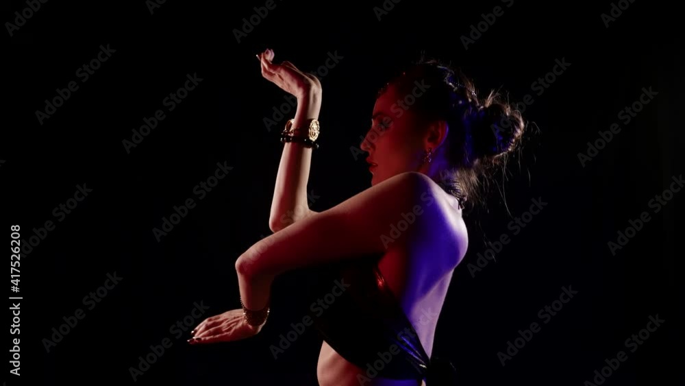 A woman who dances an oriental dance against a dark background in a studio, she is dressed in a revealing costume and is illuminated by light. A woman who dances an oriental dance against a dark background in a studio, she is dressed in a revealing costume and is illuminated by light.