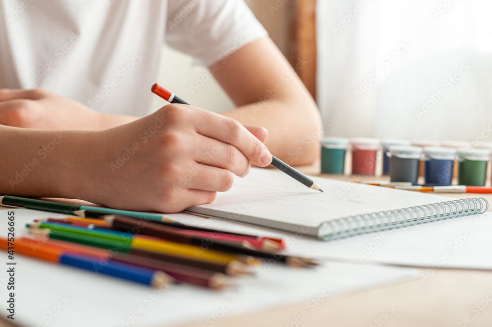 A teenage child draws. The hand of a teenage boy with a pencil. Creative hobby. Drawing lesson. Close-up and selective focus. A teenage child draws. The hand of a teenage boy with a pencil. Creative hobby. Drawing lesson. Close-up and selective focus.
