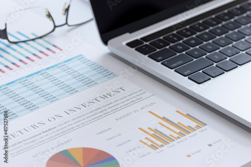 Closeup of laptop or notebook computer and financial reports with colorful charts, graphs and diagrams for business performace and return on investment, ROI, analysis