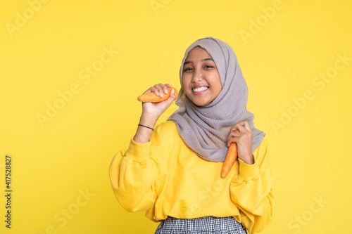 woman making fun with a carrot isolated on yellow background. © faishalabdula