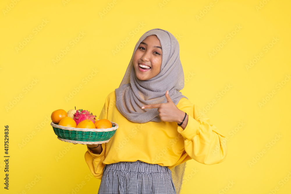 Happy asian woman holding straw basket with healthy fruits on yellow background. Happy asian woman holding straw basket with healthy fruits on yellow background.