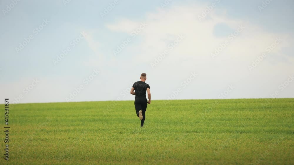 A sportsman is quickly running across the green grass. Running training. 4K. A sportsman is quickly running across the green grass. Running training. 4K.