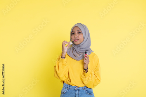 Asian young woman showing skincare products on yellow background. © faishalabdula