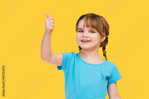 happy child girl showing thumbup isolated on yellow background 