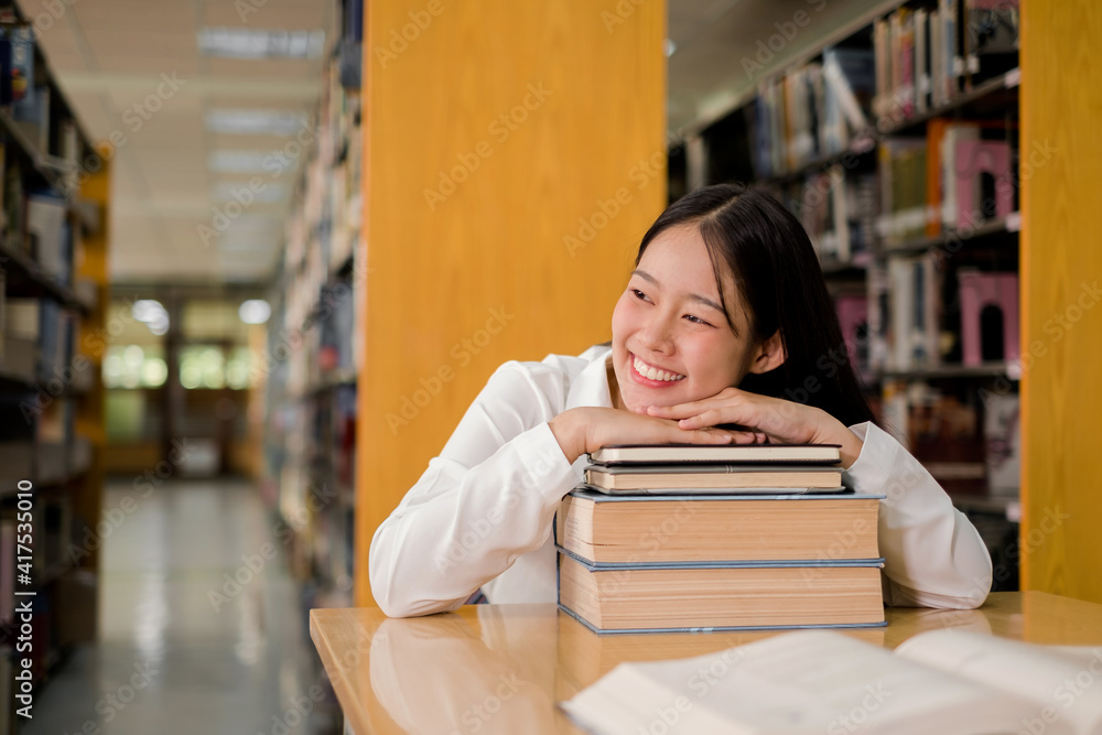 Young Asian women are searching for books and reading books on the tables and aisles of the college libraries to research and develop their academic and education self Young Asian women are searching for books and reading books on the tables and aisles of the college libraries to research and develop their academic and education self