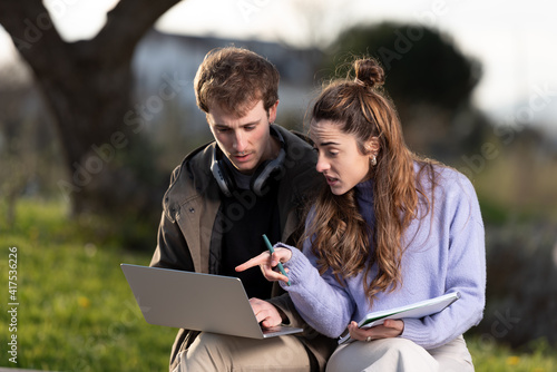 Young man and woman entrepreneurs working together on a laptop outdoors in a park with a beautiful sunset light.