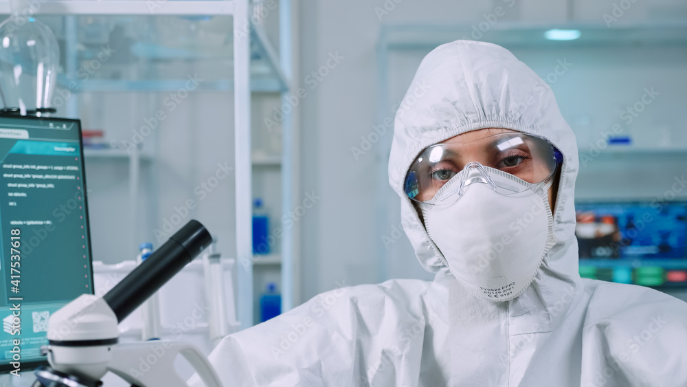 Professional woman scientist in protection suit looking tired at camera in equipped lab. Overworked team examining virus evolution using high tech and tools for scientific research vaccine development Professional woman scientist in protection suit looking tired at camera in equipped lab. Overworked team examining virus evolution using high tech and tools for scientific research vaccine development