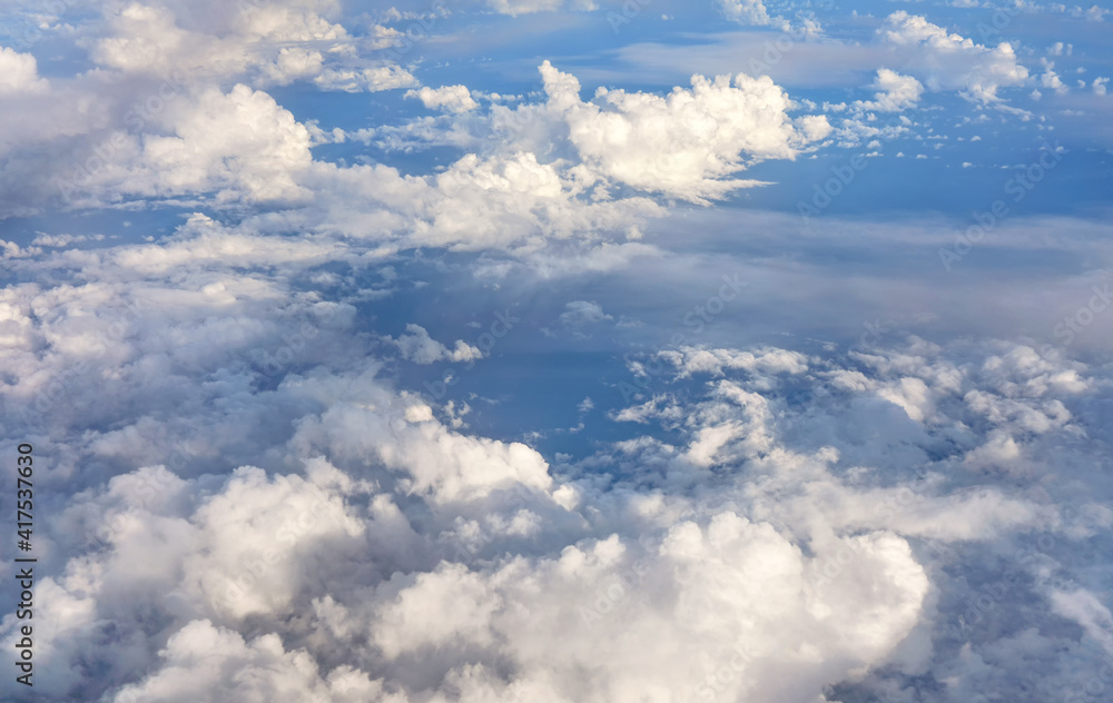 Fluffy sky clouds lit by afternoon sun, as seen from commercial airplane flying over Fluffy sky clouds lit by afternoon sun, as seen from commercial airplane flying over