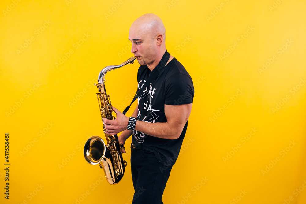 Naklejka premium Man plays the saxophone in the studio on a yellow background