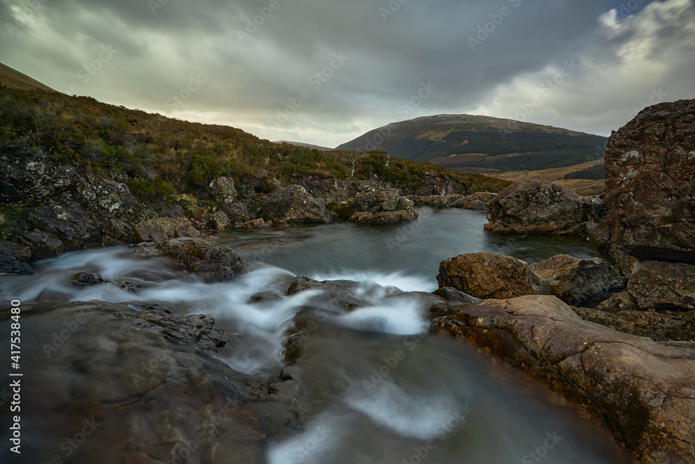 waterfall with silky water towards mountain with cloudy sky- Fairy Pools - Skye Island - Scotland - Uk waterfall with silky water towards mountain with cloudy sky- Fairy Pools - Skye Island - Scotland - Uk
