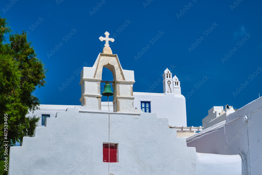 Typical bell tower or small belfry of a whitewashed Greek Orthodox church on a clear summer day. Greek island. Blue sky, no clouds. Upshot.