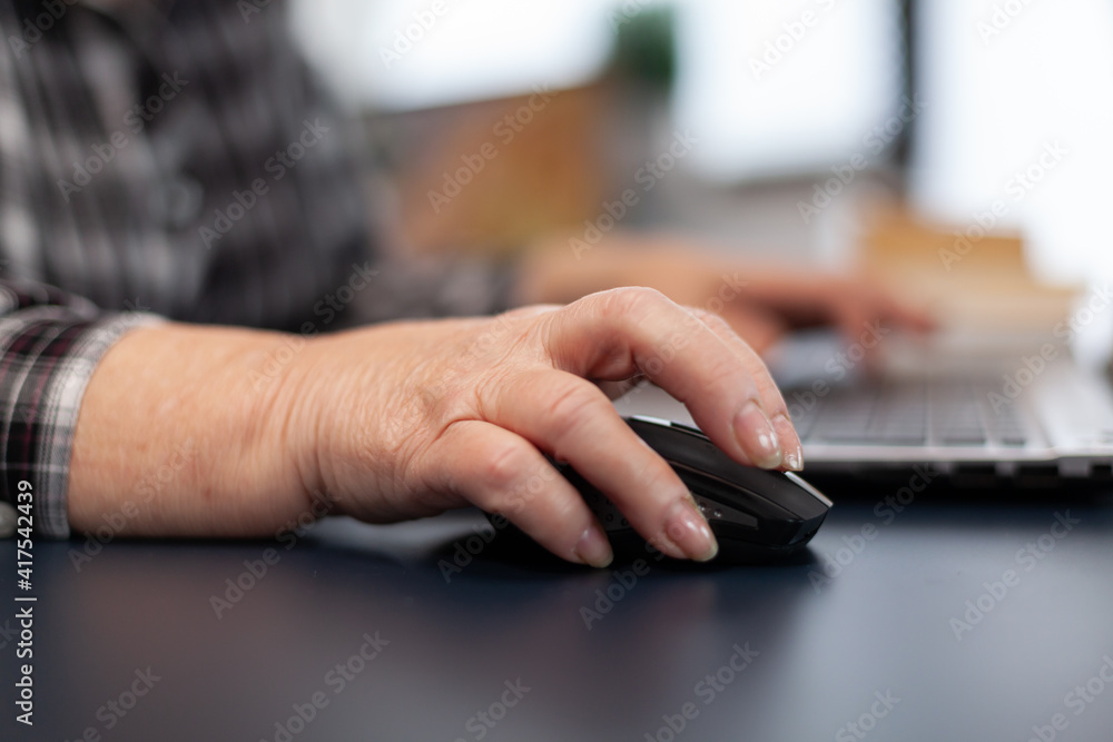 Close up of old entrepreneur lady using mouse in home office. Elderly woman in home living room using moder technoloy laptop for communication sitting at desk indoors. Close up of old entrepreneur lady using mouse in home office. Elderly woman in home living room using moder technoloy laptop for communication sitting at desk indoors.