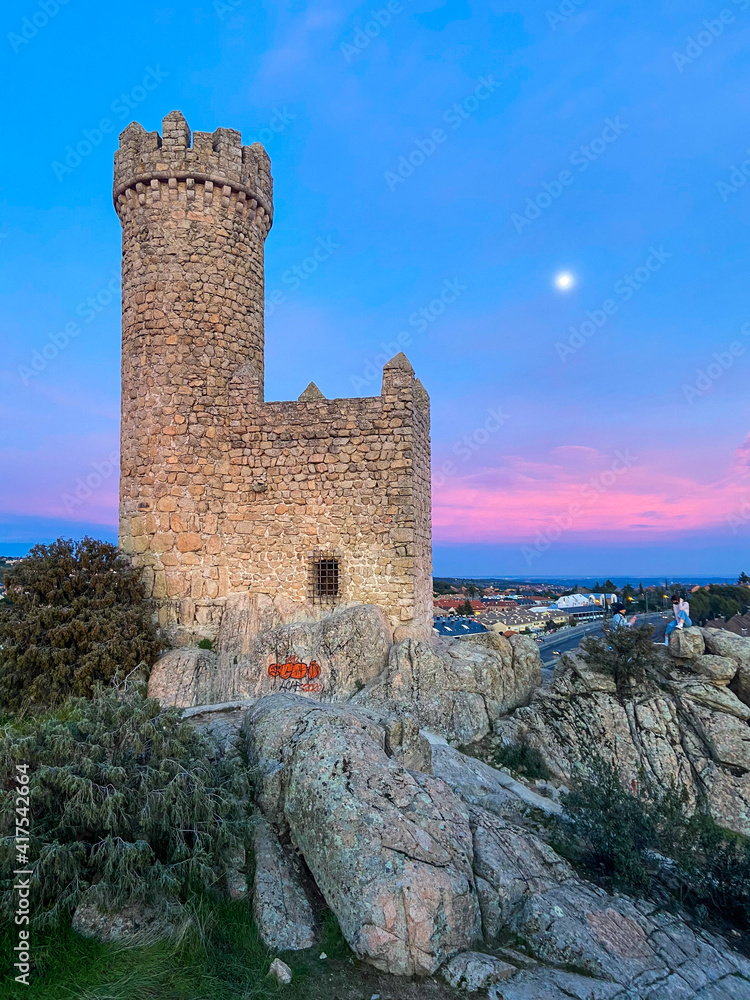 Medieval castle with full moon and colorful sunset in the background.
