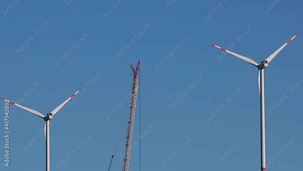 modern wind turbines and a wind turbine construction crane on a hill from far modern wind turbines and a wind turbine construction crane on a hill from far
