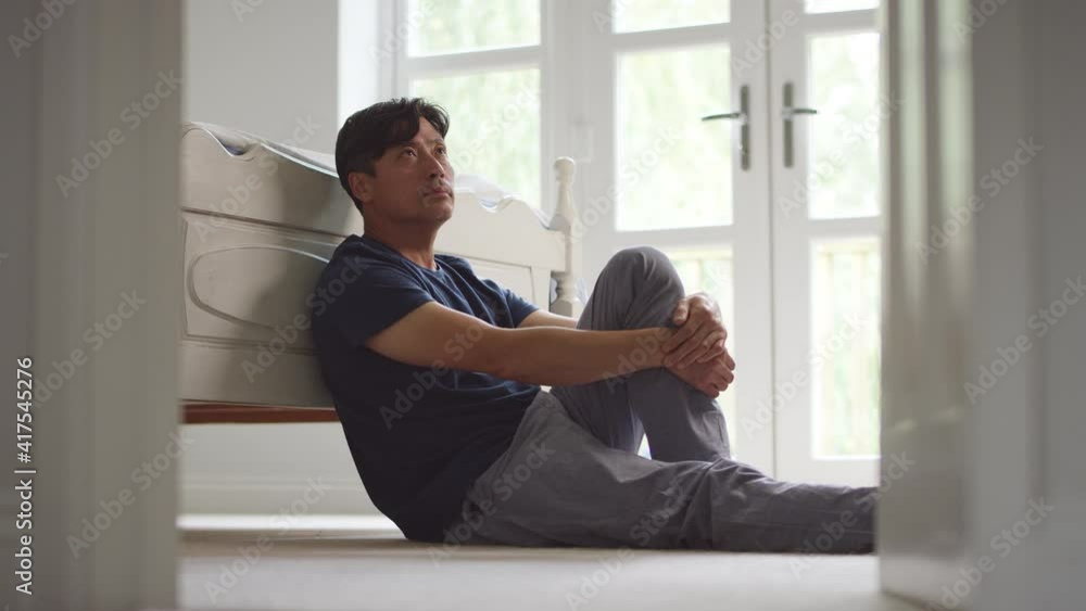 Unhappy and depressed mature Asian man wearing pyjamas sitting on floor in bedroom - shot in slow motion Unhappy and depressed mature Asian man wearing pyjamas sitting on floor in bedroom - shot in slow motion