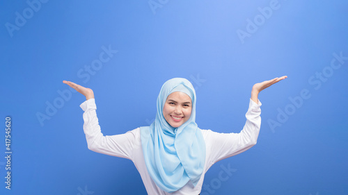 Portrait of a young muslim woman with hijab over blue background studio.