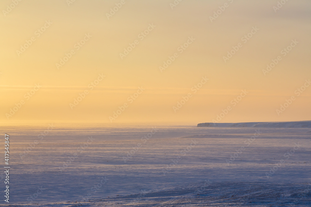 Winter arctic landscape. Morning aerial view of snowy tundra and frozen sea. In the distance is a cape. Cold windy and frosty weather. Chukotka, Polar Siberia, the Far North of Russia. Northern nature