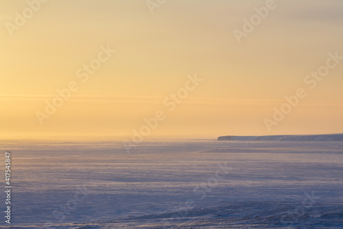 Winter arctic landscape. Morning aerial view of snowy tundra and frozen sea. In the distance is a cape. Cold windy and frosty weather. Chukotka, Polar Siberia, the Far North of Russia. Northern nature © Andrei Stepanov