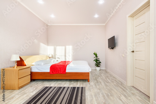 Front view of bright bedroom interior with tv  white sheet on bed  two lamps on nightstands  and day sunlight falling from window. Rostov-on-Don  Russia - 10 november 2020