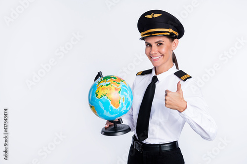 Portrait of beautiful cheerful pilot girl holding in hands globe showing thumbup advert isolated over white color background