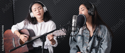 Asian female singer with a passion for music and microphone. While playing her guitar in a professional studio. Music concept, sound recording concept.