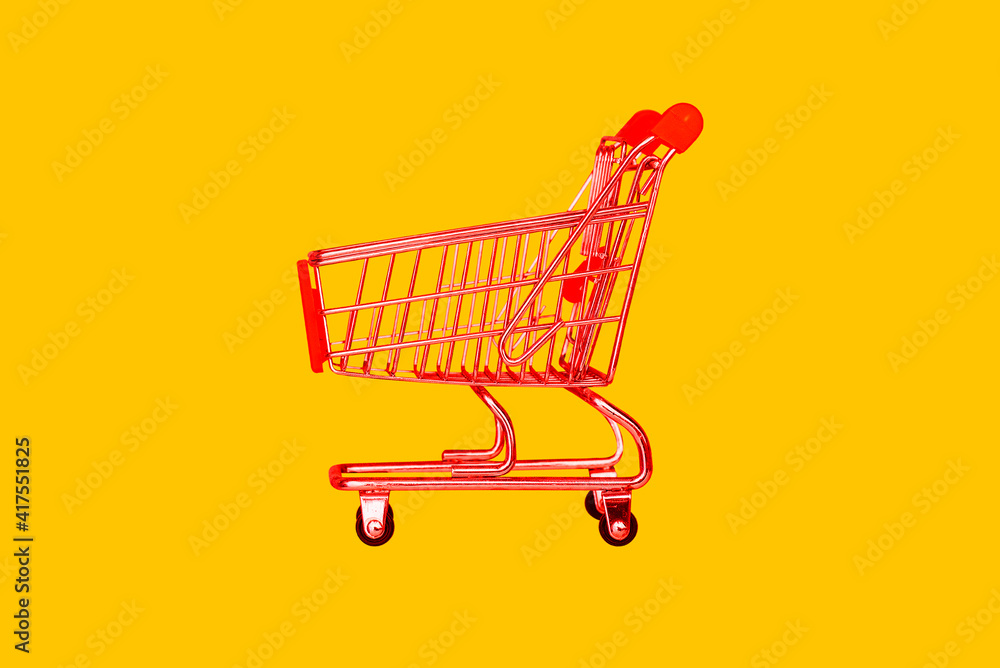 Shopping trolley in the store. Red basket on a yellow background. The concept of retail, sale of goods and products. Food trolley. Food delivery by courier from the supermarket