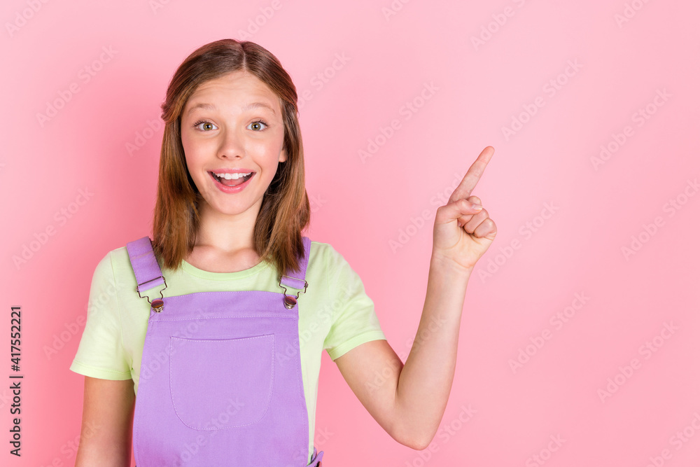 Photo portrait of little surprised girl pointing finger empty space smiling isolated on pastel pink color background Photo portrait of little surprised girl pointing finger empty space smiling isolated on pastel pink color background