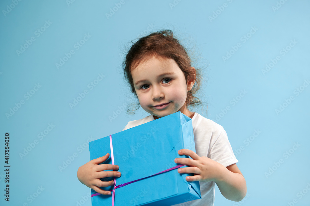 Adorable girl with blue gift on blue background with copy space. Children Day. Birthday concept. Adorable girl with blue gift on blue background with copy space. Children Day. Birthday concept.