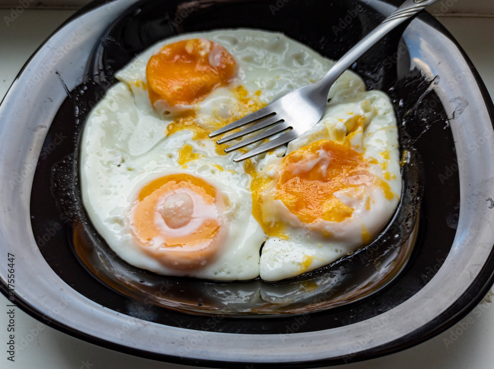 photo of fried eggs in a black plate on a white background. food photo