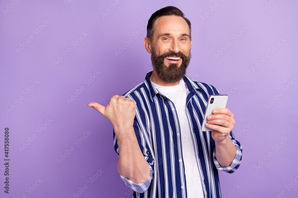 Photo of adviser guy hold telephone indicate thumb empty space wear striped shirt isolated purple color background Photo of adviser guy hold telephone indicate thumb empty space wear striped shirt isolated purple color background