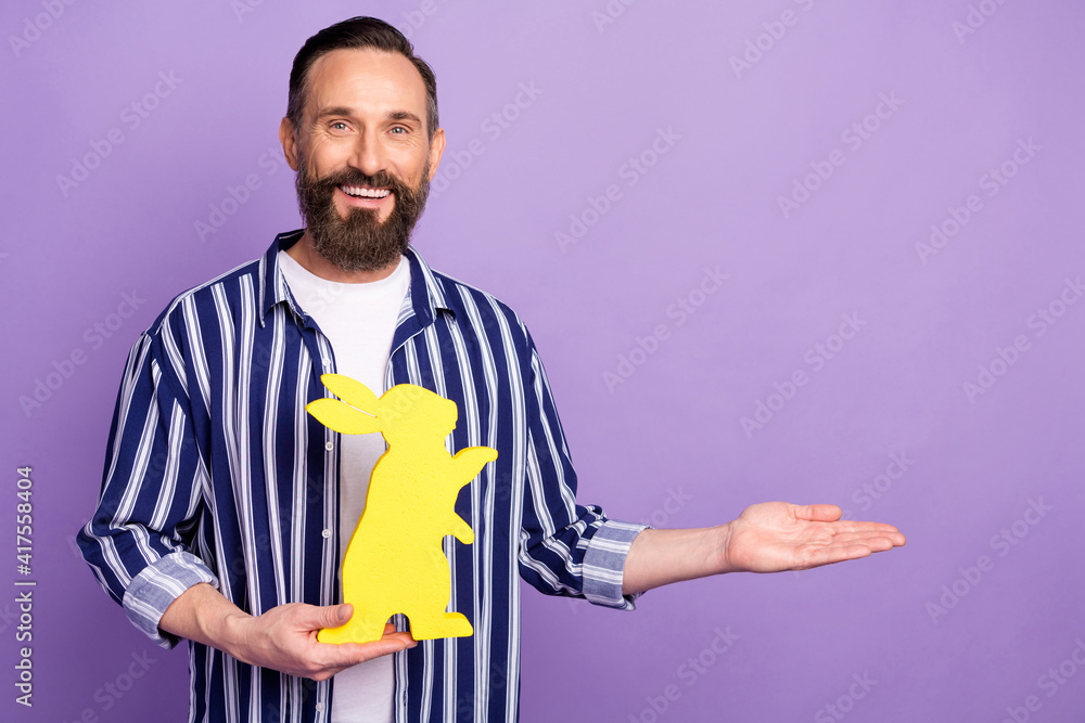 Photo of guy hold yellow hare figure hand hold empty space wear striped shirt isolated purple color background Photo of guy hold yellow hare figure hand hold empty space wear striped shirt isolated purple color background
