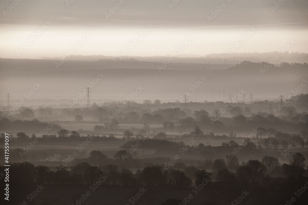 sunrise casts a golden glow on the rising mist filled Pewsey Vale from Martinsell Hill, Wiltshire