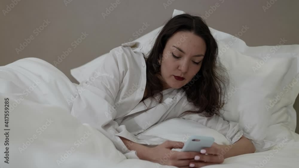 young woman is chatting by messenger app in smartphone at morning, lying in bed after wake up