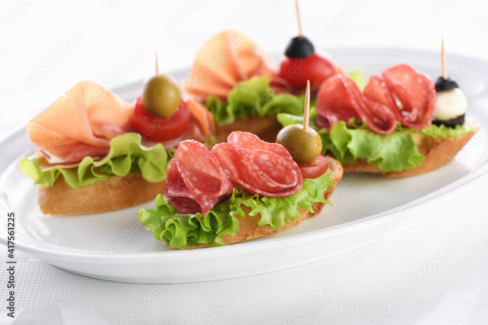  Tender baguette canapes with Leaf lettuce, salami or Parma ham, tomatoes, mozzarella and olive. Delicacy assorted platter for at the party.