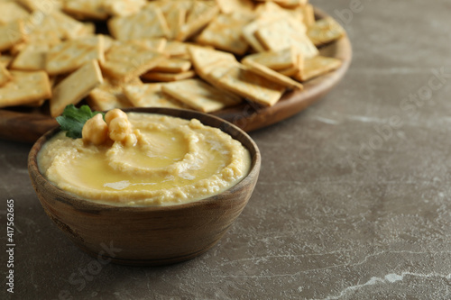 Tray with crackers and bowl of hummus on gray background