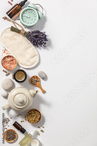 Herbal medicine for treat depression and insomnia concept. Alarm clock, medicine herbs, capsules, camomile tea and aromatherapy oil on white background, flat lay photo