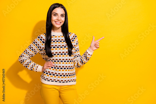 Photo of young beautiful lovely happy positive smiling girl pointing finger copyspace isolated on yellow color background