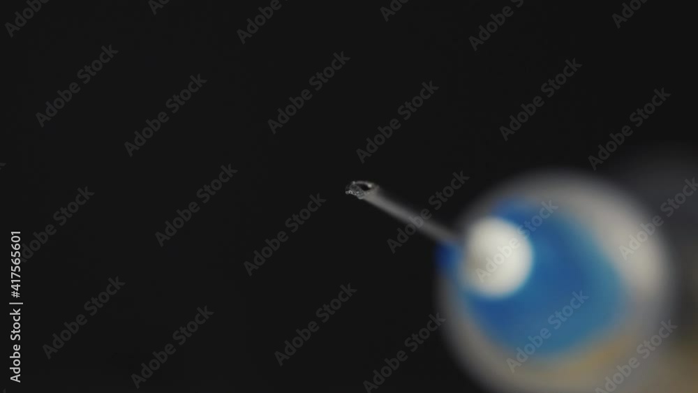 A medical syringe with a vaccine dripping from a needle. Reflection in a drop. Close-up. A medical syringe with a vaccine dripping from a needle. Reflection in a drop. Close-up.