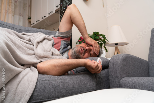 Male model with high fever flu symptoms resting on sofa at home