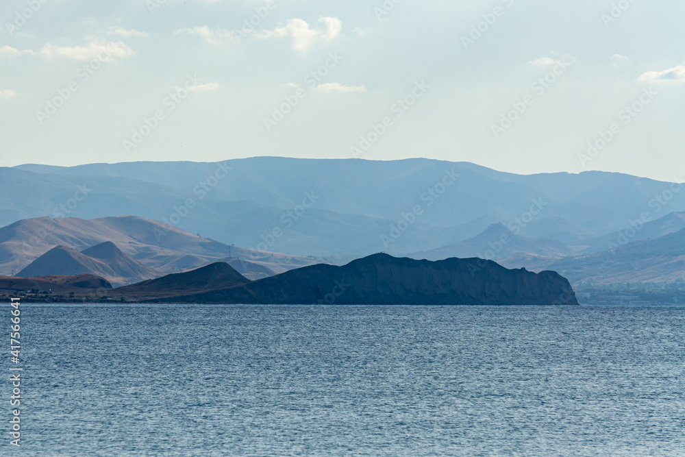 Beautiful landscape with rocky coastline on horizon. Panoramic view. Mountains of Black Sea coast of Crimea from height of ridge between Feodosia and Koktebel. Shtil at sea. Sun at sunset.