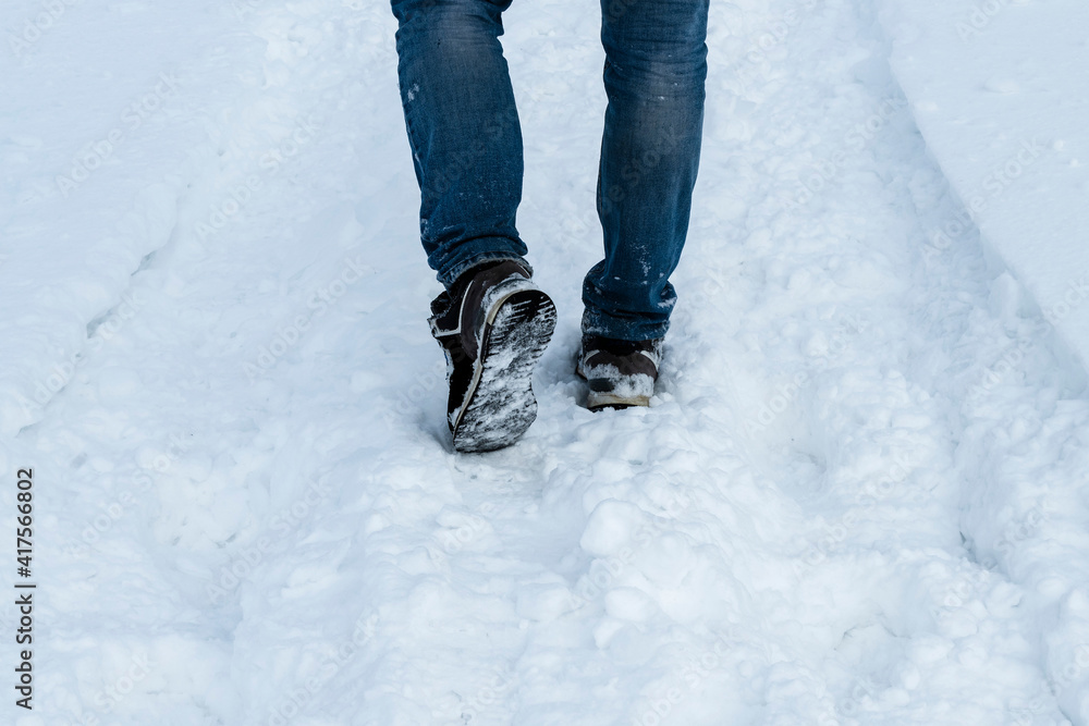 The legs of a man in blue jeans and snow-covered black sneakers on a snow trail close-up. Photo for an article about winter hiking. The legs of a man in blue jeans and snow-covered black sneakers on a snow trail close-up. Photo for an article about winter hiking.