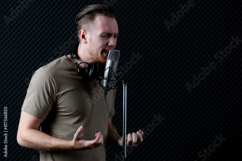 Young and handsome male singer working in voice recording studio, he sings to microphone with deep emotion and intention. Taken with studio light in dark style