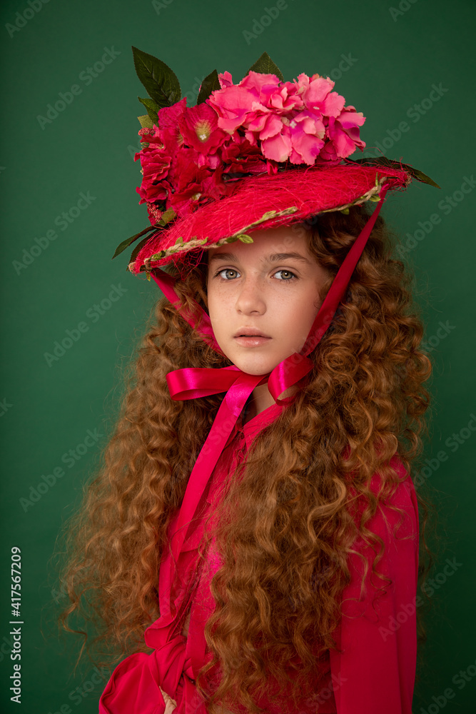 Redhair beautiful girl with curly afro curls in bright pink dress on green background. Curly hair care, freckle cream, teen book cover. Close-up fashion portrait. Art hat flowers Redhair beautiful girl with curly afro curls in bright pink dress on green background. Curly hair care, freckle cream, teen book cover. Close-up fashion portrait. Art hat flowers
