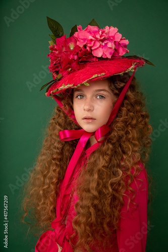 Redhair beautiful girl with curly afro curls in bright pink dress on green background. Curly hair care, freckle cream, teen book cover. Close-up fashion portrait. Art hat flowers © Татьяна Волкова
