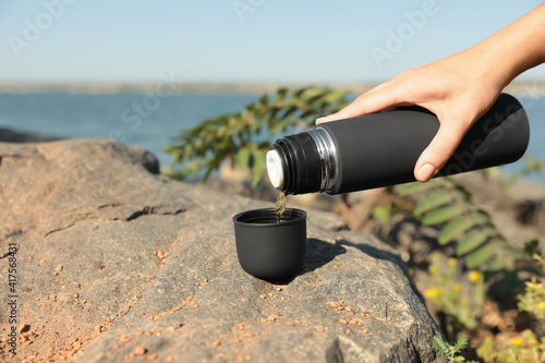 Woman pouring hot drink from thermos into cap outdoors, closeup