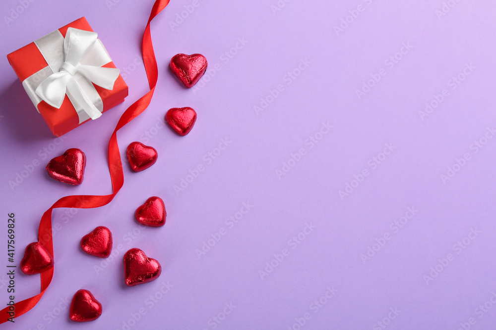 Heart shaped chocolate candies, ribbon and gift box  on violet background, flat lay. Space for text