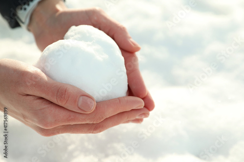 Woman holding heart made of snow outdoors, closeup. Space for text